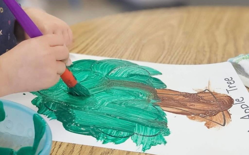 Child painting an apple tree art project at Sunny Pointe